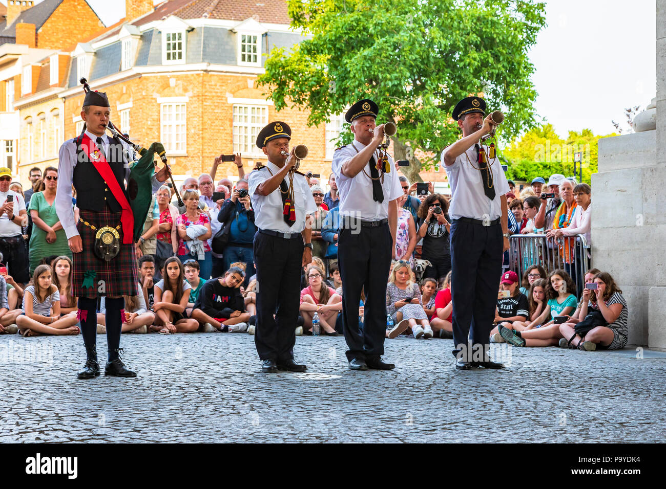 Three buglers standing to attention while a lone piper plays a lament at the Menin Gate war memorial, Ypres, Belgium Stock Photo