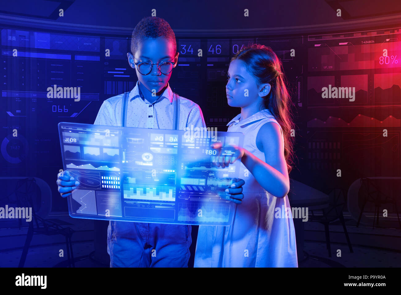 Serious boy holding a transparent device and a girl pointing at it Stock Photo