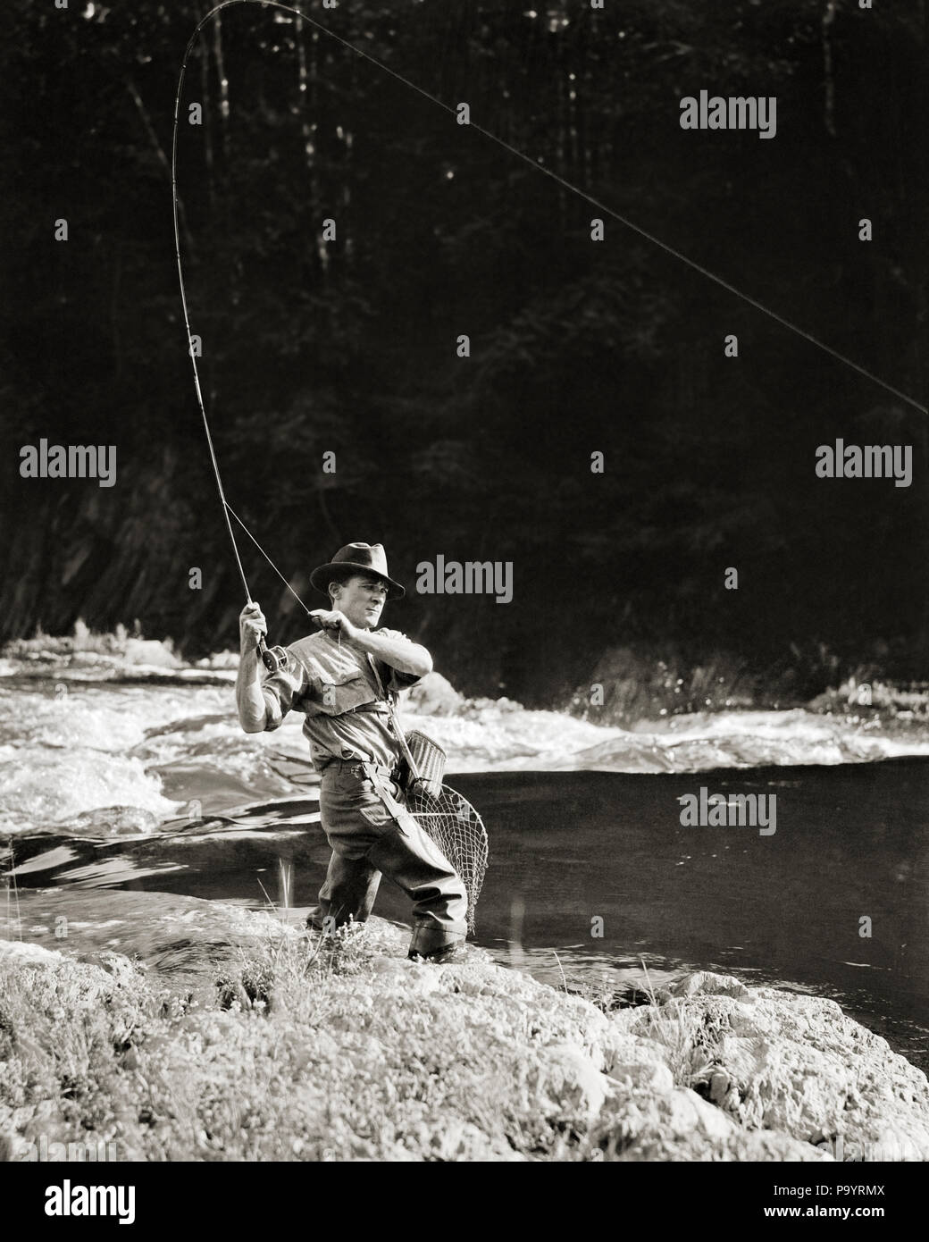 1920s MAN ANGLER FLY FISHING CASTING WITH ROD REEL CREEL AND LANDING NET -  a454 HAR001 HARS SPIRITUALITY ANGLER B&W FREEDOM ACTIVITY DREAMS HAPPINESS  PHYSICAL STRENGTHENING ADVENTURE LEISURE STRENGTH SELF ESTEEM EXCITEMENT