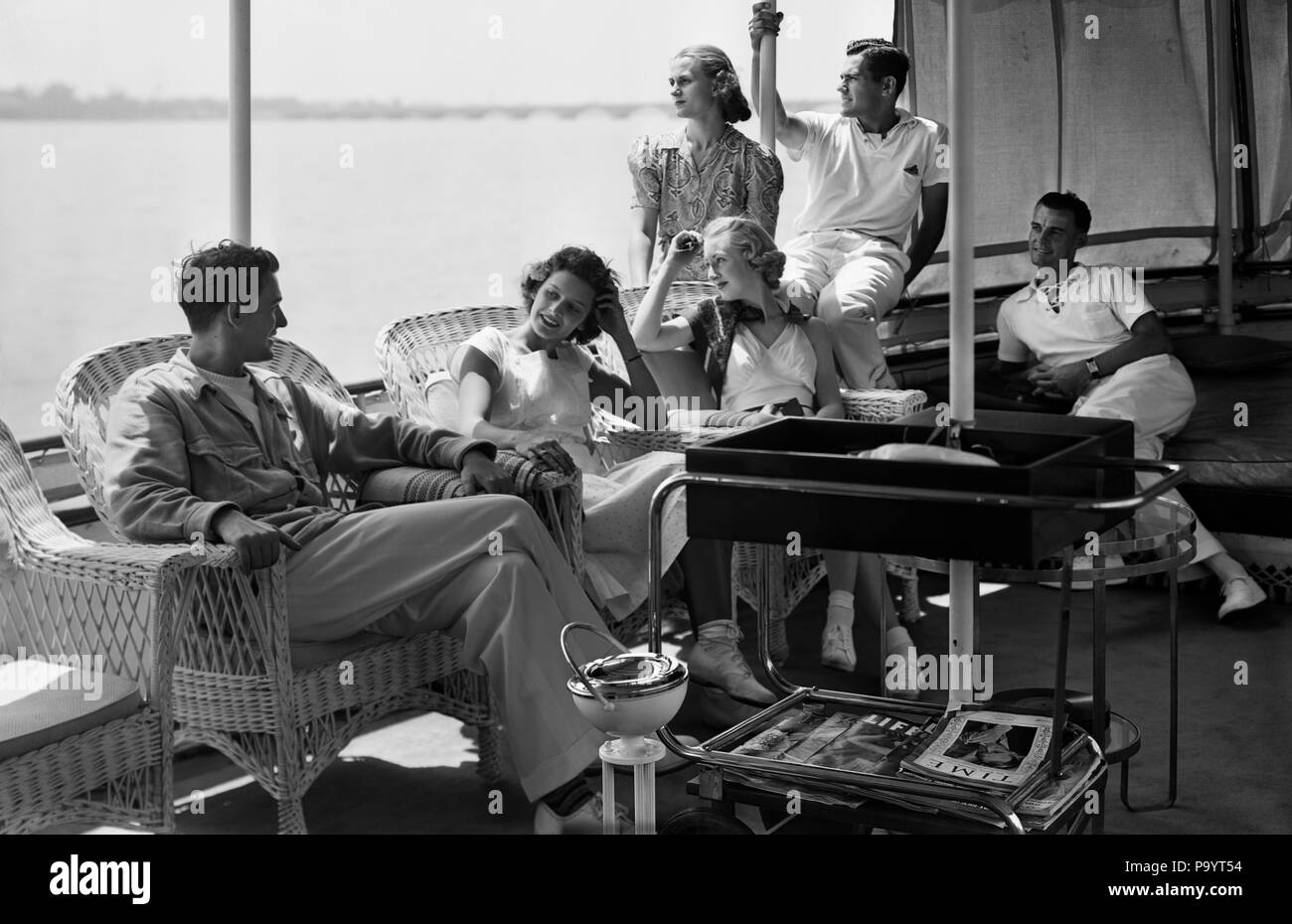 1930s GROUP MEN WOMEN ONBOARD YACHT RELAXING ON SHADED DECK - bx005638 CAM001 HARS COPY SPACE FRIENDSHIP HALF-LENGTH LADIES PERSONS WICKER MALES SHADE B&W TIME OFF DREAMS HAPPINESS LEISURE GETAWAY SOCIETY WEALTH CAM001 HOLIDAYS TRAVELING UPSCALE ESCAPE STYLISH SHADED MID-ADULT RELAXATION TOGETHERNESS VACATIONS WIVES BLACK AND WHITE CAUCASIAN ETHNICITY COMPANIONS FIRST CLASS OLD FASHIONED Stock Photo