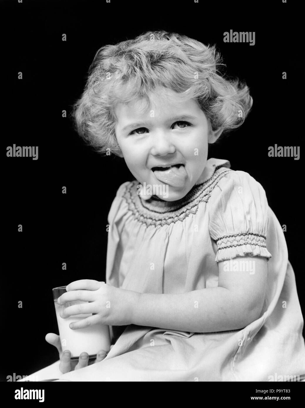 1920s 1930s SMILING LITTLE GIRL CURLY SHORT HAIR HOLDING GLASS OF MILK LOOKING AT CAMERA LICKING HER LIPS WITH TONGUE DELICIOUS - f524 HAR001 HARS EXPRESSIONS B&W EYE CONTACT LICKING HAPPINESS BEVERAGE STRENGTH CURLY NOURISHMENT GROWTH JUVENILES TASTY BLACK AND WHITE CAUCASIAN ETHNICITY DELICIOUS HAR001 OLD FASHIONED Stock Photo