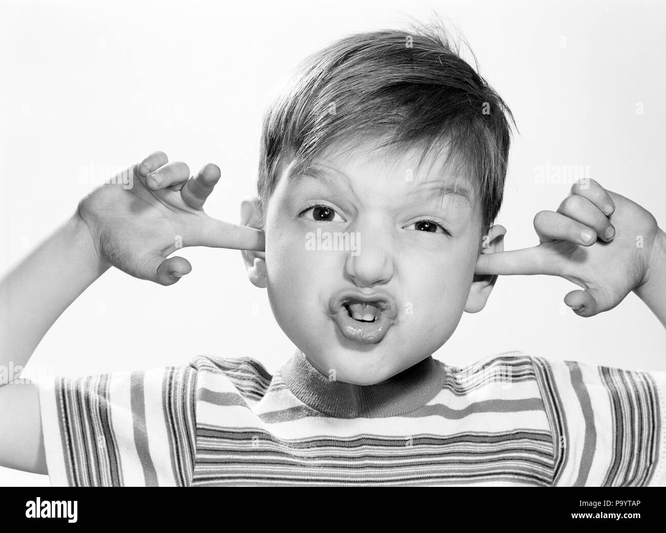 1960s SURPRISED ALARMED DISTRESSED BOY WEARING STRIPED T-SHIRT LOOKING AT CAMERA STICKING INDEX FINGERS IN HIS EARS - j11763 DEB001 HARS RISK EXPRESSIONS B&W EYE CONTACT INDEX COMPLAINING WEIRD HEAD AND SHOULDERS DISCOVERY DISTRESSED EXCITEMENT LOUD ZANY STICKING UNCONVENTIONAL IN BOTHERED UNCOMFORTABLE DEB001 IDIOSYNCRATIC T-SHIRT AMUSING ECCENTRIC JUVENILES PEACE AND QUIET ALARMED BLACK AND WHITE CAUCASIAN ETHNICITY ERRATIC OLD FASHIONED Stock Photo