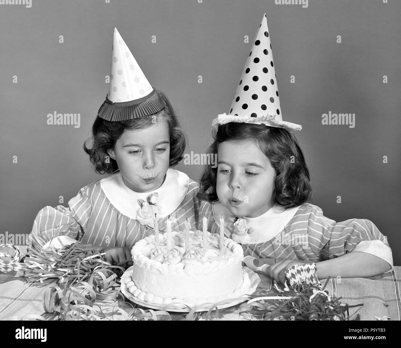 1960s TWIN GIRLS WEARING PARTY HATS BLOWING OUT CANDLES ON BIRTHDAY CAKE - j12268 HAR001 HARS HALF-LENGTH INSPIRATION MATCH CARING SIBLINGS SPIRITUALITY SISTERS B&W MATCHING SAME HAPPINESS HEAD AND SHOULDERS EXCITEMENT RECREATION SIBLING STYLISH LOOK-ALIKE DUPLICATE GROWTH JUVENILES LOOK ALIKE TOGETHERNESS BLACK AND WHITE CAUCASIAN ETHNICITY CLONE HAR001 OLD FASHIONED Stock Photo