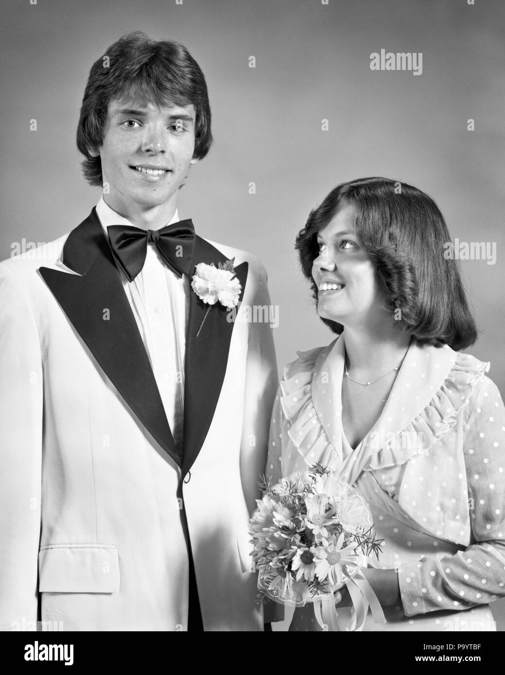 1970s TEEN COUPLE DRESSED UP FOR PROM DANCE FORMAL ATTIRE GIRL HOLDING BOUQUET LOOKING UP AT TALL BOY - j13789 HAR001 HARS JOY LIFESTYLE CELEBRATION FRIENDSHIP HALF-LENGTH INSPIRATION TEENAGE GIRL TEENAGE BOY CONFIDENCE EXPRESSIONS B&W EYE CONTACT DREAMS HAPPINESS CHEERFUL EXCITEMENT AT HIGH SCHOOL SMILES HIGH SCHOOLS CONNECTION JOYFUL STYLISH ATTIRE DRESSED UP GROWTH LOOKING UP TOGETHERNESS BLACK AND WHITE CAUCASIAN ETHNICITY HAR001 OLD FASHIONED Stock Photo