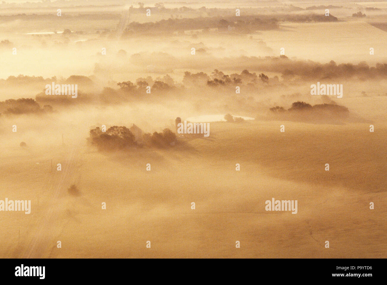 AERIAL VIEW OF FARM IN EARLY MORNING FOG NEAR EDGERTON KANSAS USA - ka5844 GLE001 HARS CALM FOUL BAD WEATHER BEIGE DREAMY FOUL WEATHER LOOKING DOWN OVERHEAD VIEW SILO TAN AERIAL VIEW AERIALS CLOUDY MIDWEST MOISTURE Stock Photo