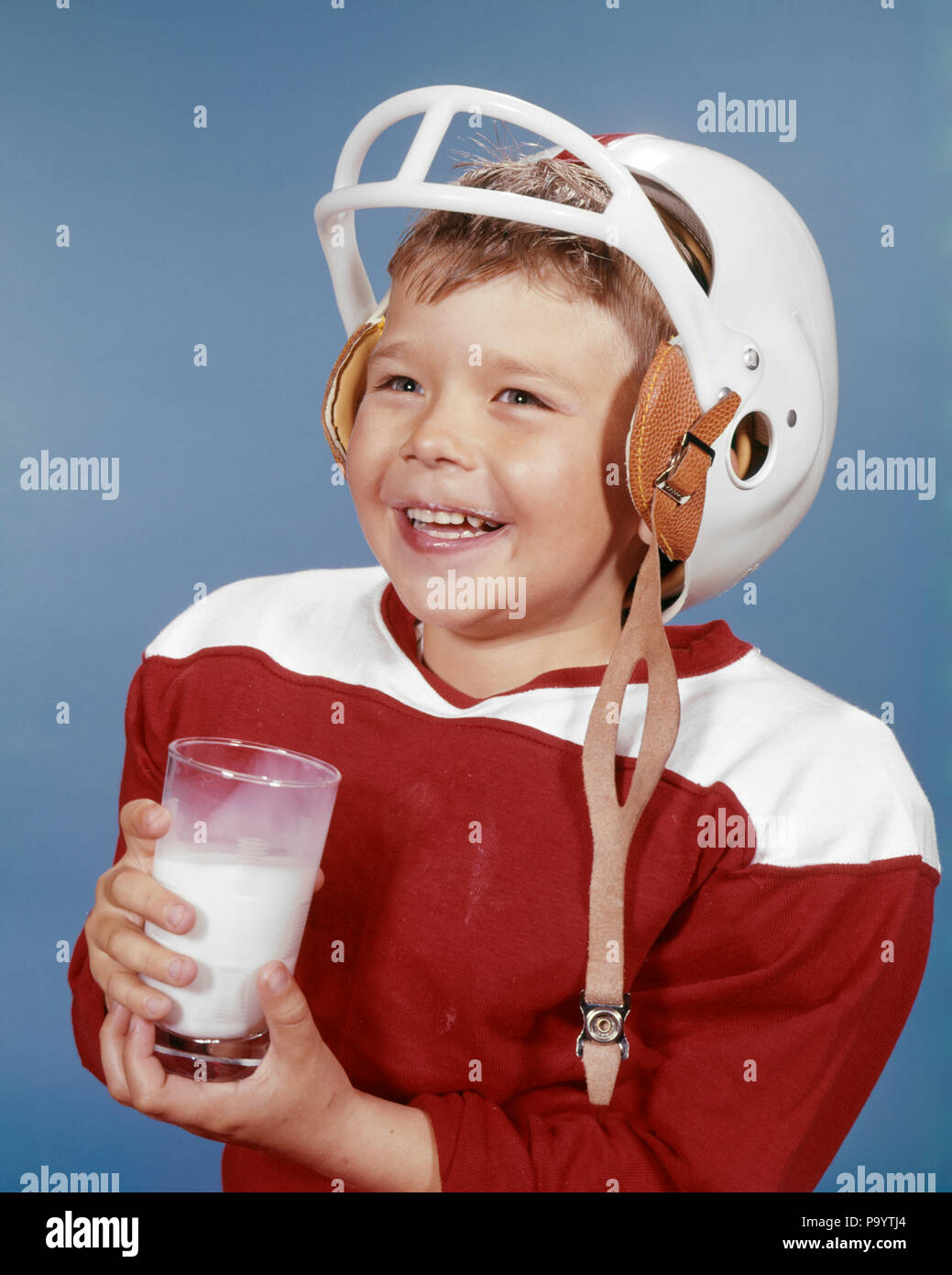 1960s SMILING BOY DRINKING MILK WEARING FOOTBALL UNIFORM AND HELMET RED JERSEY  - kf2991 HAR001 HARS PLEASED JOY HEALTHINESS HOME LIFE COPY SPACE FRIENDSHIP HALF-LENGTH PHYSICAL FITNESS MALES EXPRESSIONS HAPPINESS CHEERFUL BEVERAGE PROTECTION AND NUTRITION RECREATION SMILES JOYFUL STYLISH NUTRITIOUS GROWTH JUVENILES CAUCASIAN ETHNICITY HAR001 OLD FASHIONED Stock Photo