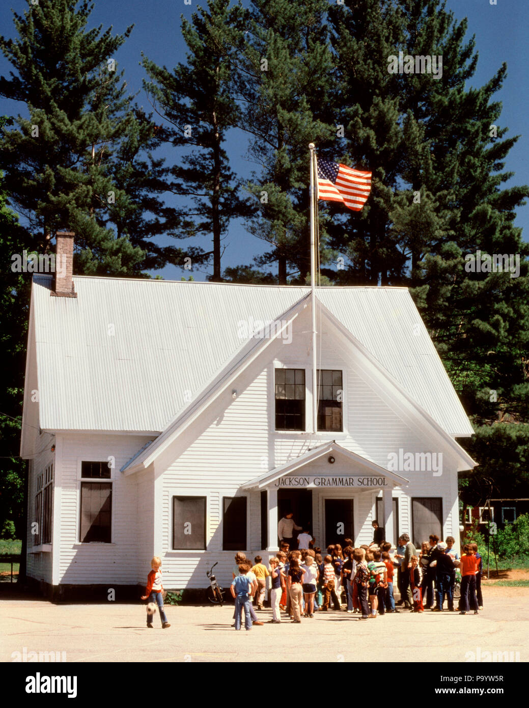 1980s CHILDREN ASSEMBLED OUTSIDE GRAMMAR SCHOOL JACKSON NEW HAMPSHIRE USA - ks17602 SEB001 HARS UNITED STATES OF AMERICA MALES BUILDINGS SUNNY AMERICANA HAMPSHIRE NORTH AMERICA GOALS SCHOOLS GRADE BRIGHT PROPERTY ENTERING EXTERIOR KNOWLEDGE RECESS PRIMARY SCHOOLHOUSE REAL ESTATE STRUCTURES ASSEMBLED EDIFICE GRAMMAR K-12 GRADE SCHOOL GROWTH JUVENILES NEW ENGLAND RED WHITE AND BLUE STARS AND STRIPS CAUCASIAN ETHNICITY JACKSON NEW HAMPSHIRE OLD FASHIONED Stock Photo