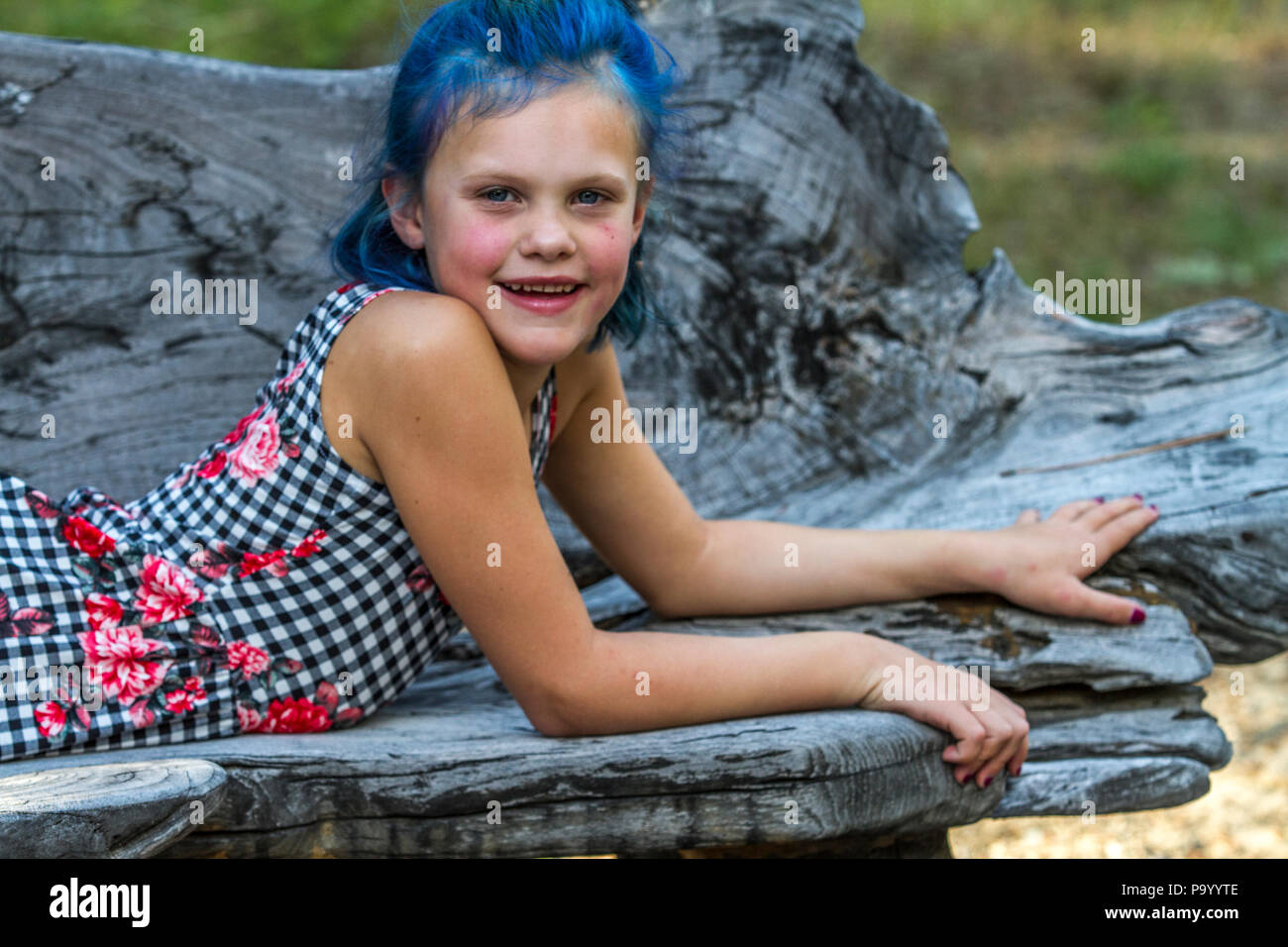 Atrtractive 8 year old girl, in colorful jump suit, hair is dyed bright blue, looking at camera and laying on bench. Model Release #113 Stock Photo