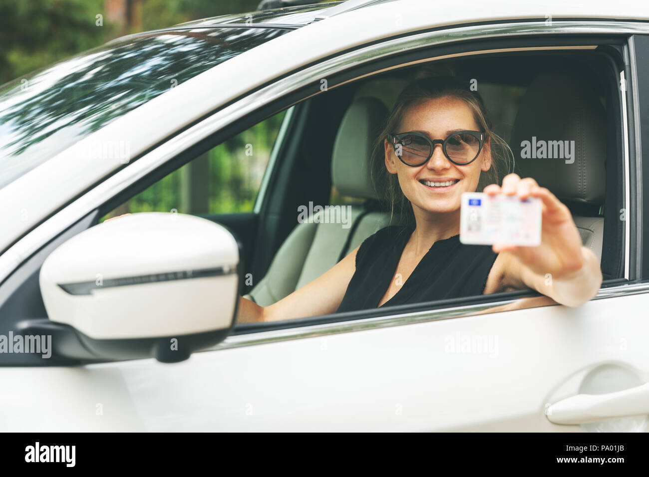 happy young woman showing her driver license through the car window Stock Photo