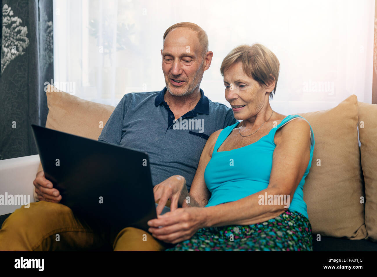 senior couple sitting in sofa and using laptop together at home Stock Photo