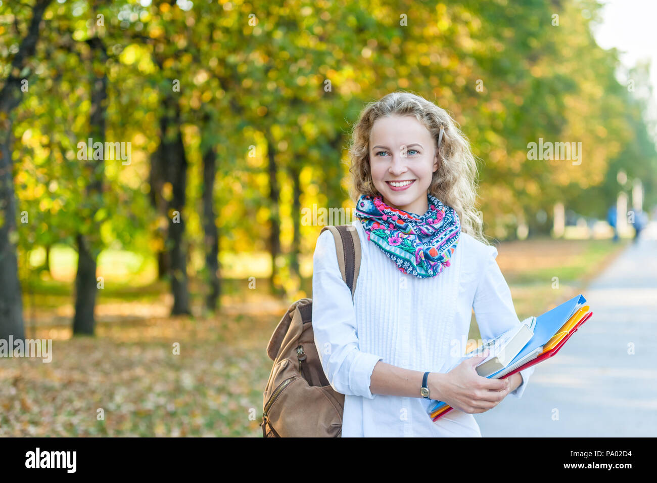 Smiling girl student with folders and books walking in the autumn park Stock Photo