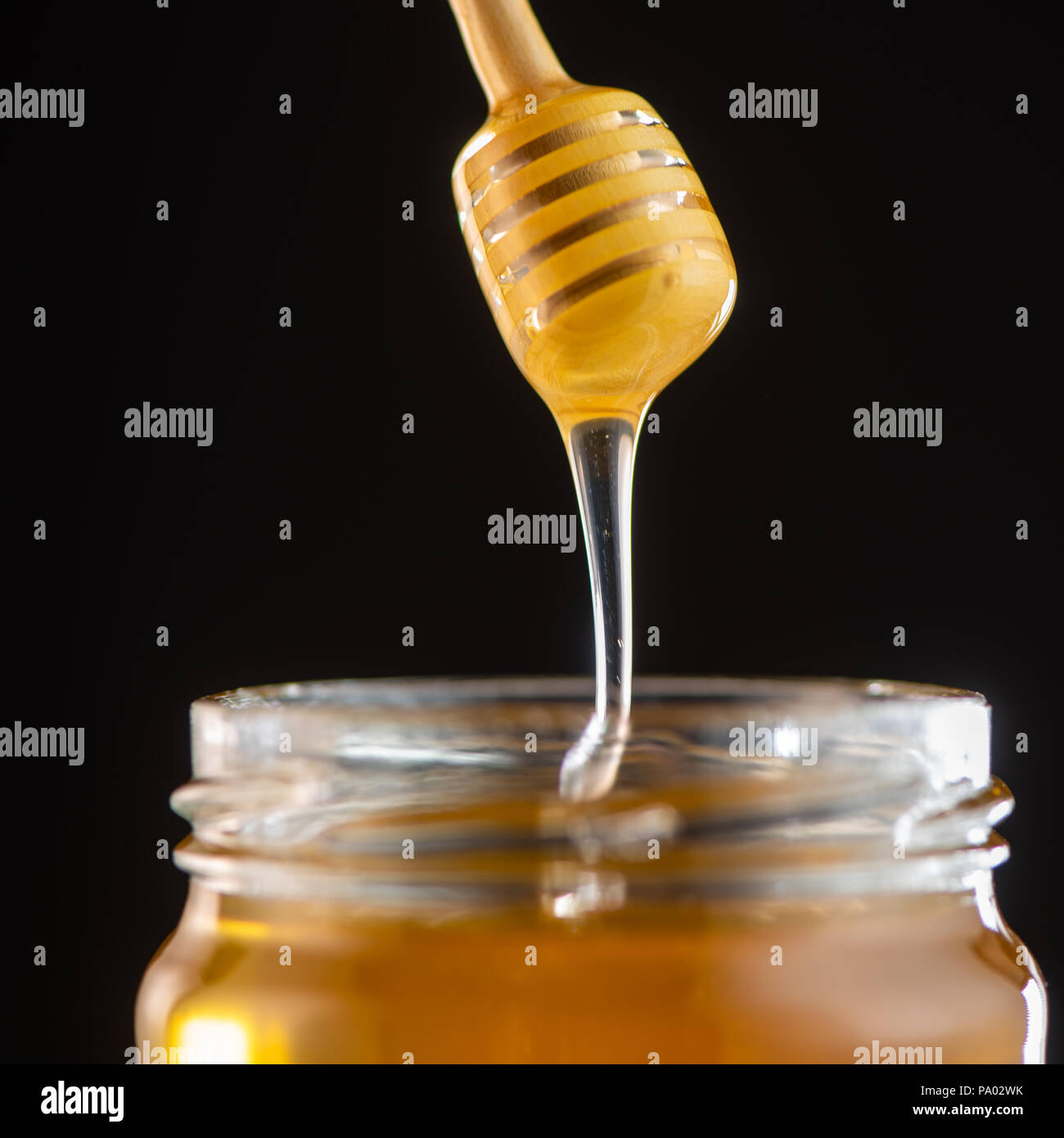 Organic honey drips from wooden dipper in jar, France Stock Photo