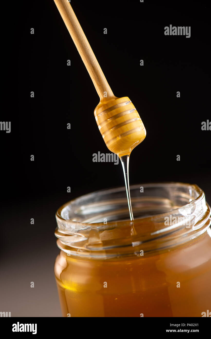 Organic honey drips from wooden dipper in jar, France Stock Photo