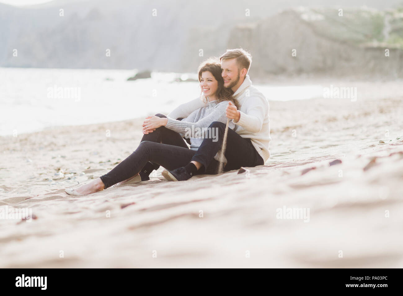 Happy man and woman sitting on sand near sea, romantic mood Stock Photo