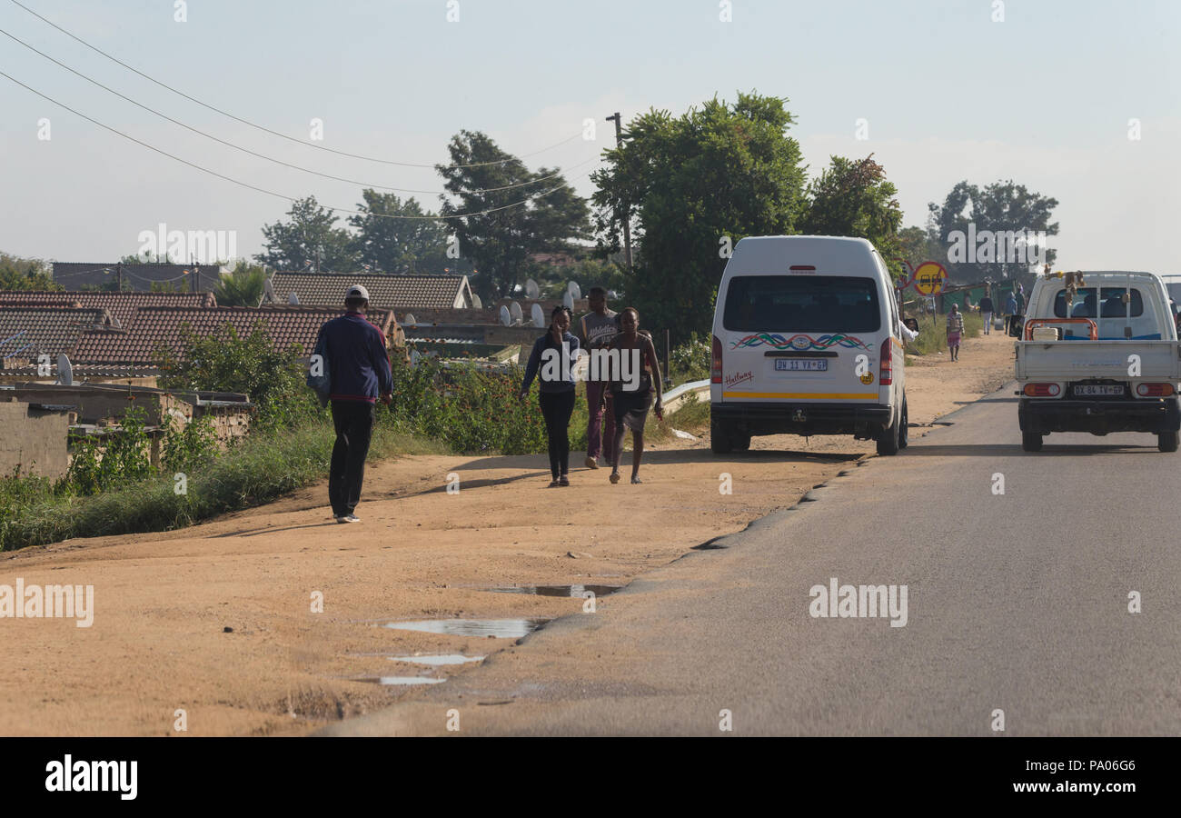 African people commuting and walking on dirt section of road in front of black taxi parked on the side of the road in Diepsloot north of Johannesburg Stock Photo