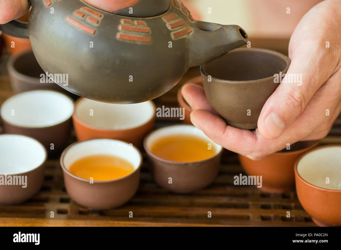 Man tea Master Host Pouring Tea into Cup from Pot at Ceremony. Chinese Japanese Set on Bamboo Wooden Tray. Freshly Brewed Beverage. Lifestyle. Wellnes Stock Photo