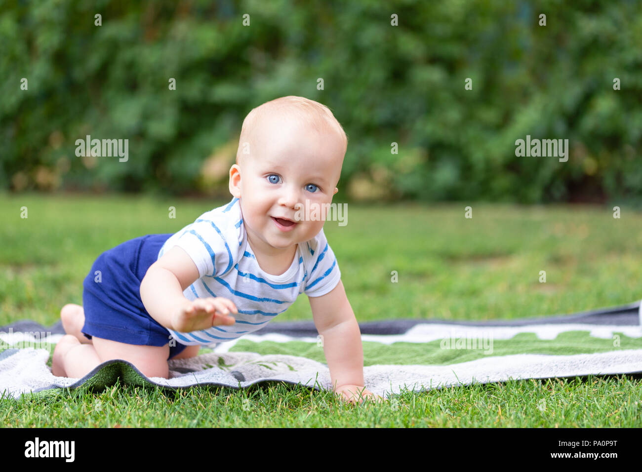 Cute little blond baby boy crawling on fresh green grass. Kid having fun making first steps on mowed natural lawn. Happy and healthy childhood concept Stock Photo