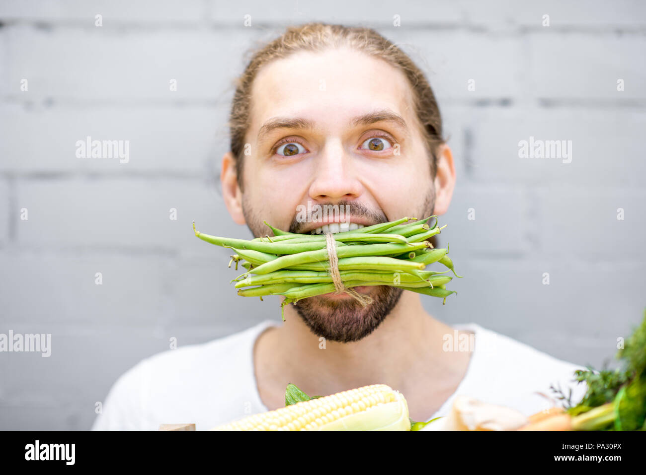 Close portrait of a handsome man biting green beans on the brick wall