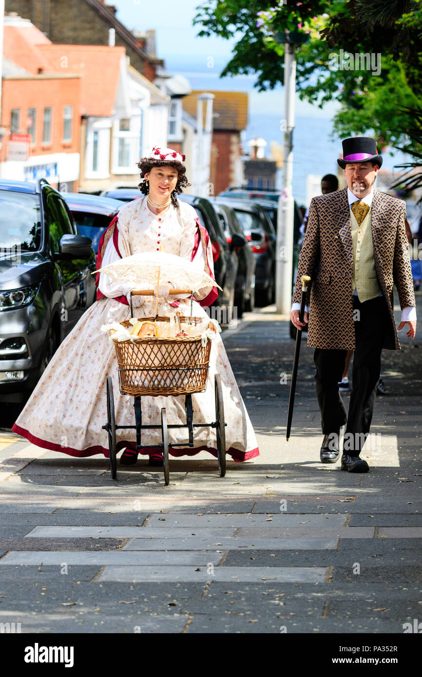 Young couple dressed in Victorian costume, walking along sunny street pushing pram, towards viewer. Part of Charles Dickens week festival, Broadstairs Stock Photo