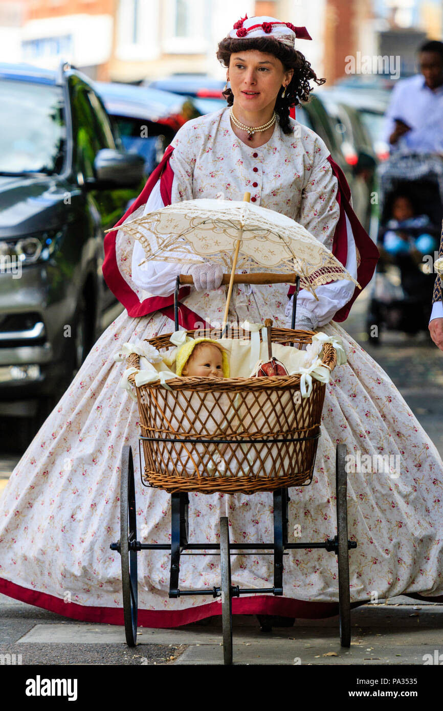 Young woman dressed in Victorian costume, walking along sunny street pushing pram, towards viewer. Part of Charles Dickens week festival, Broadstairs. Stock Photo