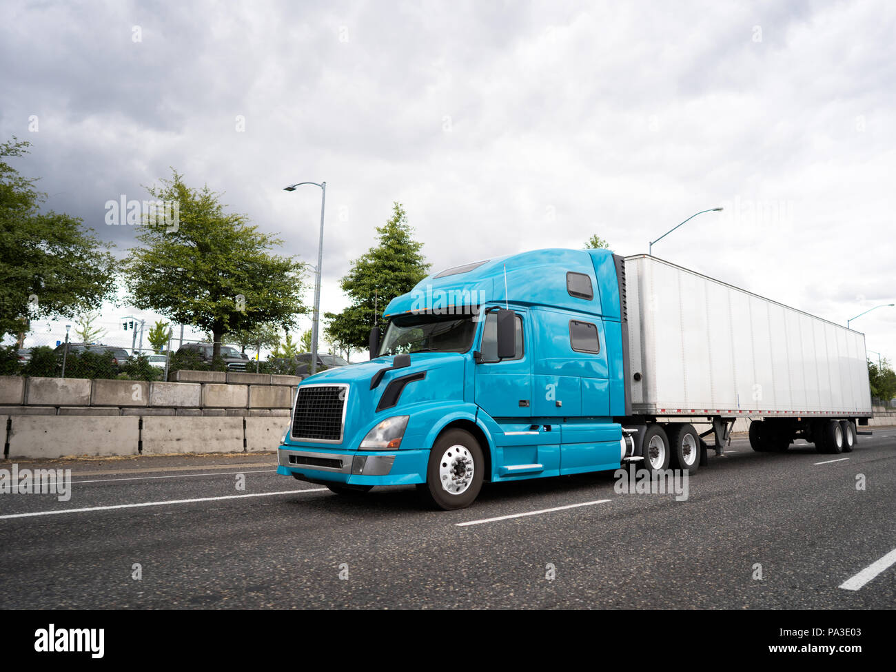 Powerful popular blue bonnet big rig semi truck with high comfortable cabin for long haul transporting industrial cargo in dry van semi trailer going  Stock Photo