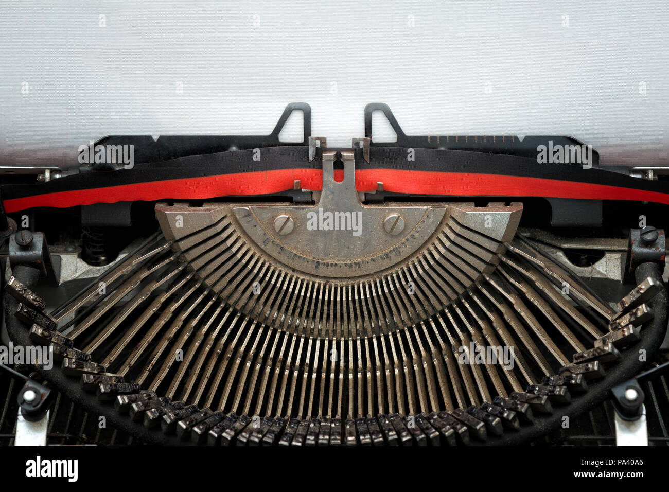 close vintage typewriter black and red ribbon and typebars ready to type on a blank textured sheet Stock Photo