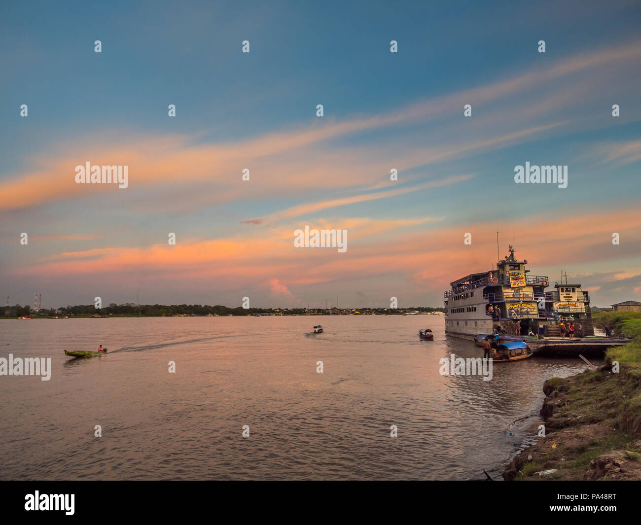 Santa Rosa, Peru - Mar 24, 2018: Sunset over the Amazon river and the cargo boat waiting at the port. Stock Photo