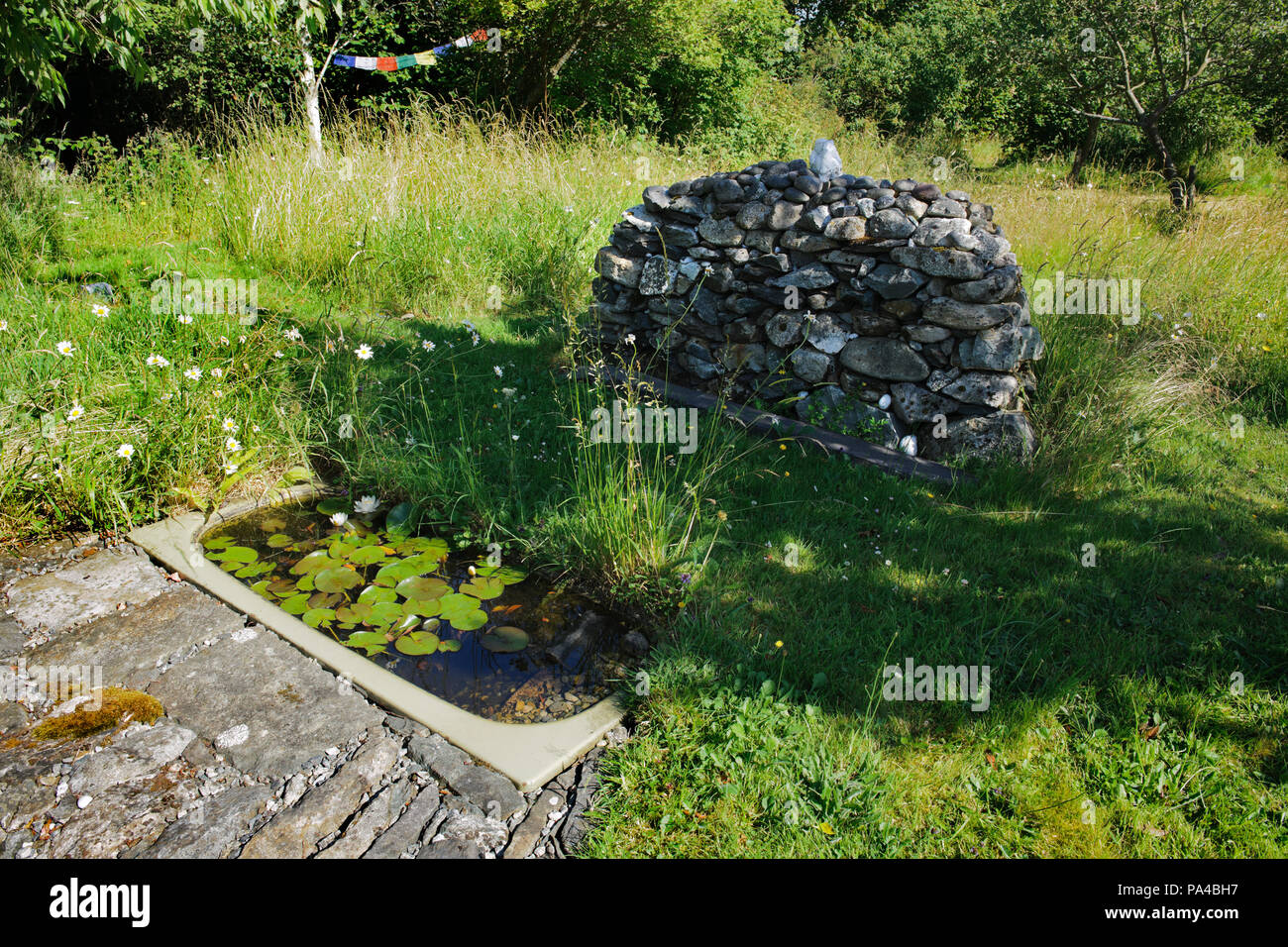 A wildlife pond, stone paving & a cairn, made using a recycled bath and masonry from a demolished extension, in a woodland garden near Caernarfon, UK. Stock Photo