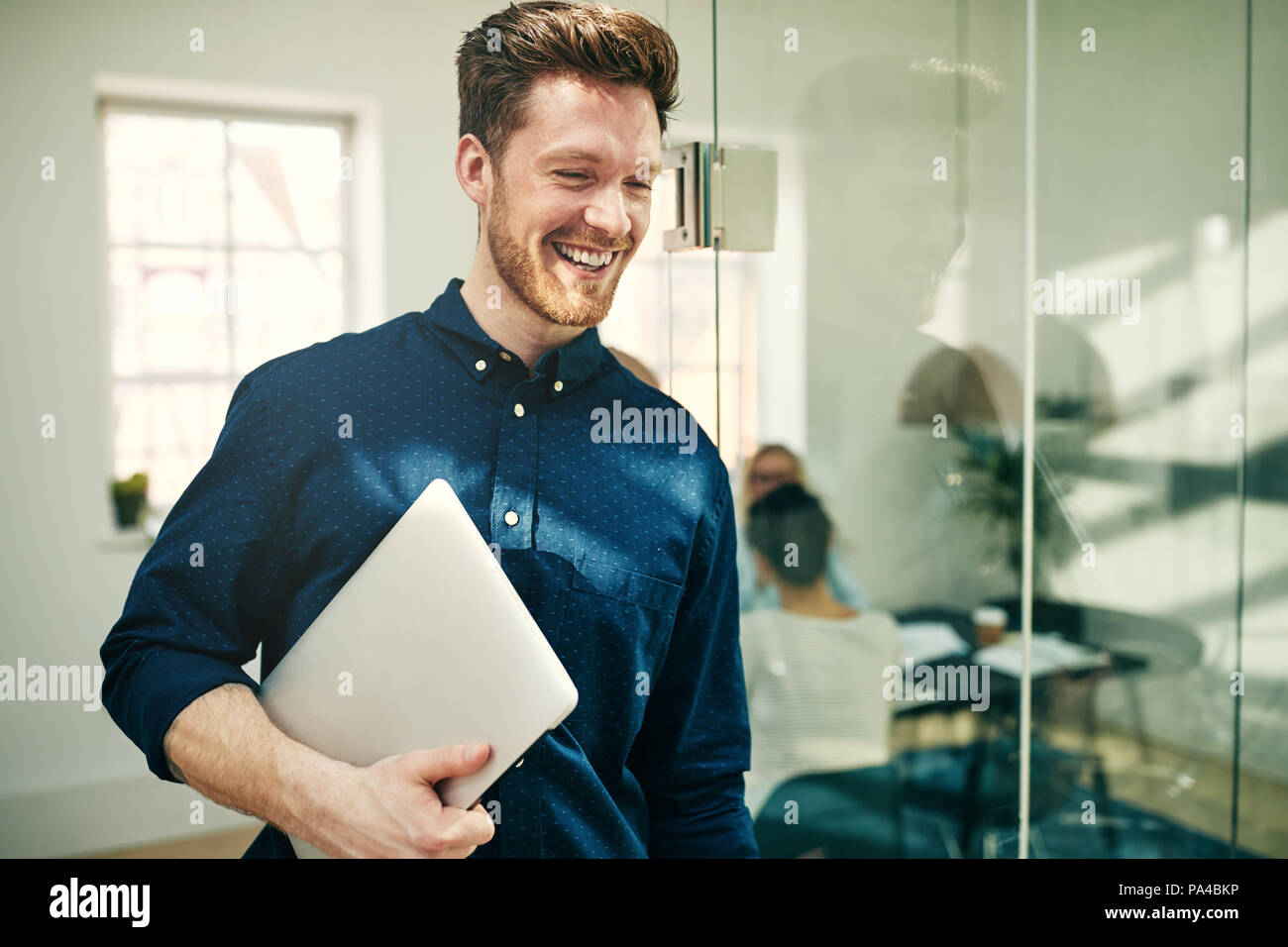 Young businessman laughing while walking in a modern office carrying a ...