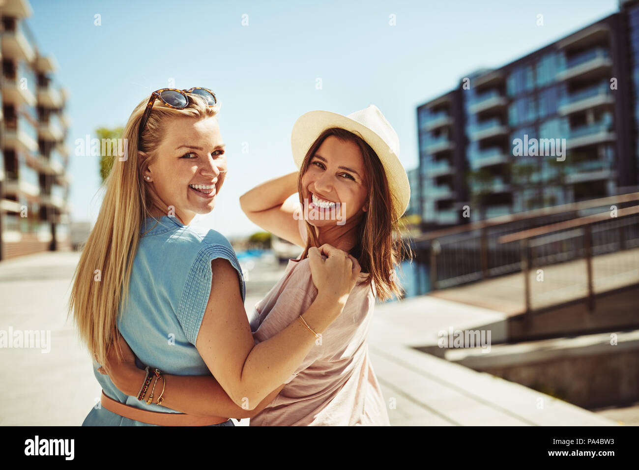 Two Carefree Young Best Friends Looking Over Their Shoulder While Walking Arm In Arm Together In The City In Summer Stock Photo Alamy