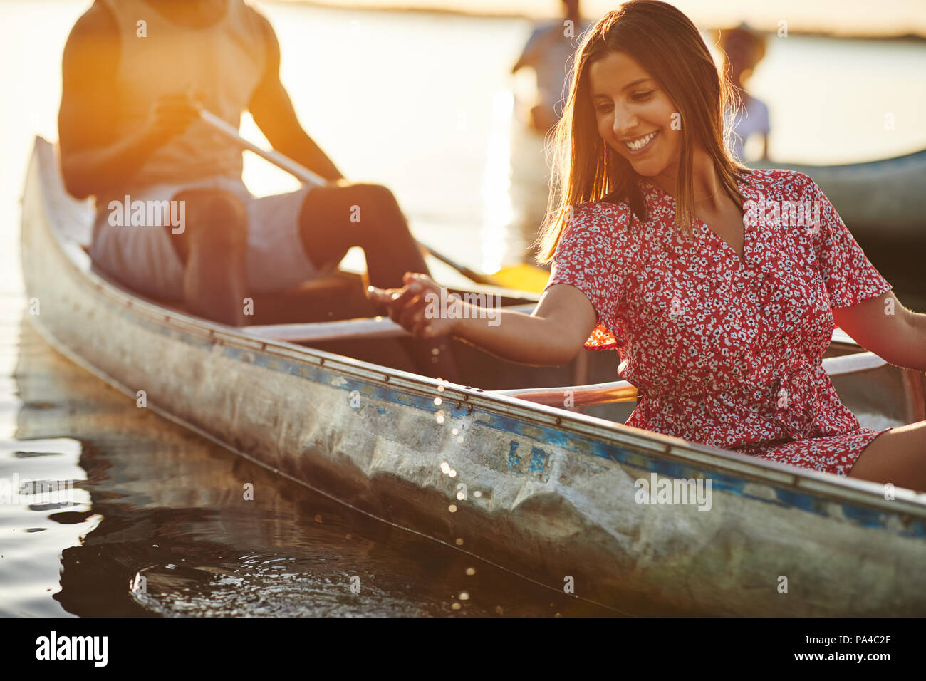 Smiling young woman dipping her hand in the water while paddling a canoe with her boyfriend on a lake on a sunny summer afternoon Stock Photo