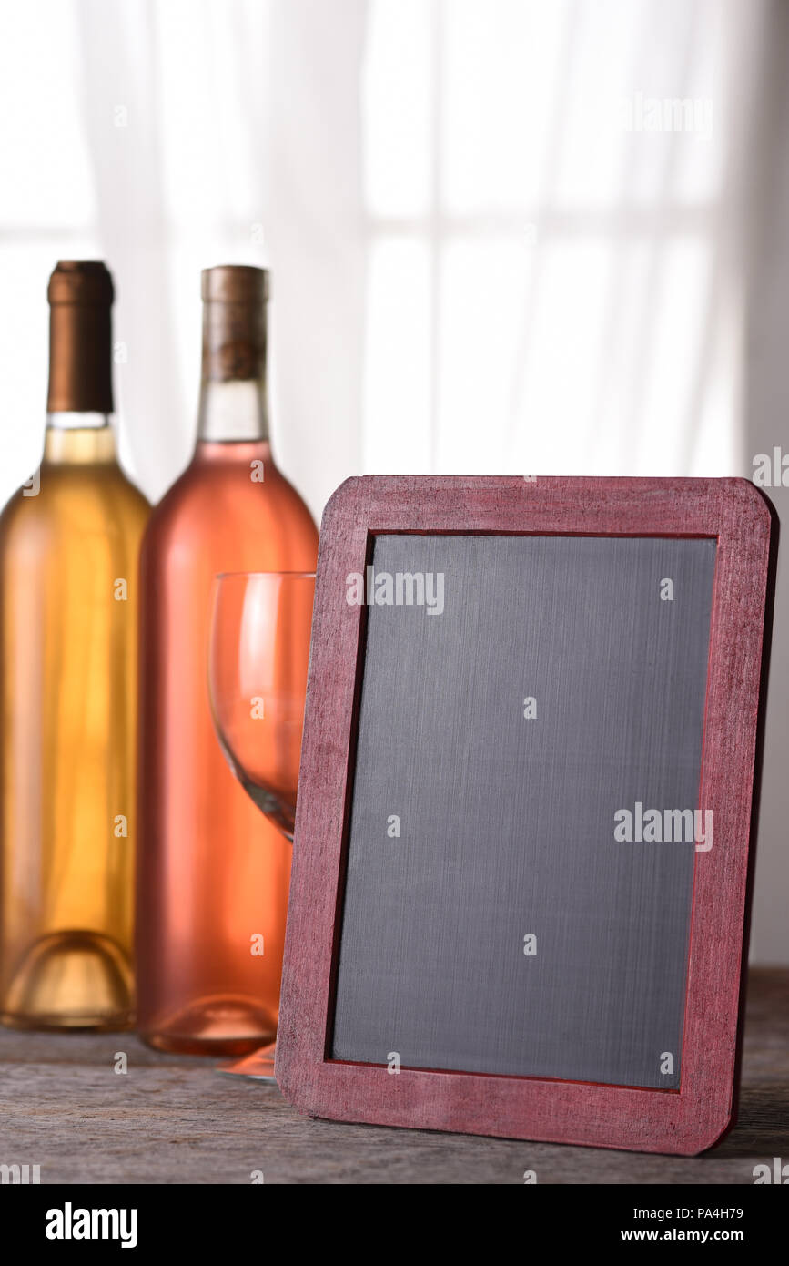 A bottle of blush and chardonnay wine with a blank menu board, on a rustic wood table in front of a window. Perfect for a Wine Menu or Wine Tasting an Stock Photo