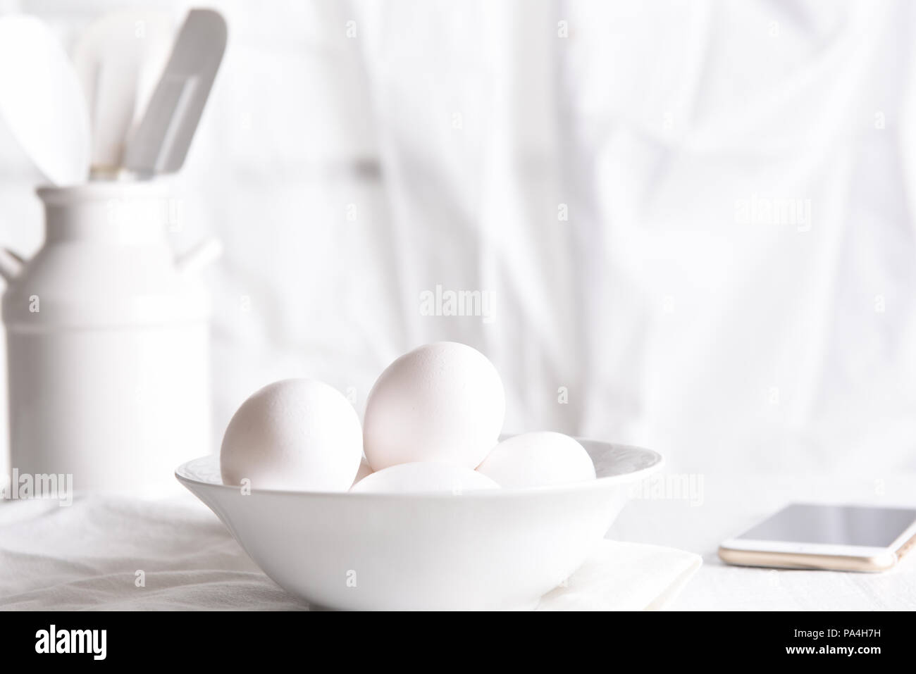 High Key Egg Still Life: Fresh eggs in a white bowl in front of a window with white curtains. Horizontal orientation. Stock Photo