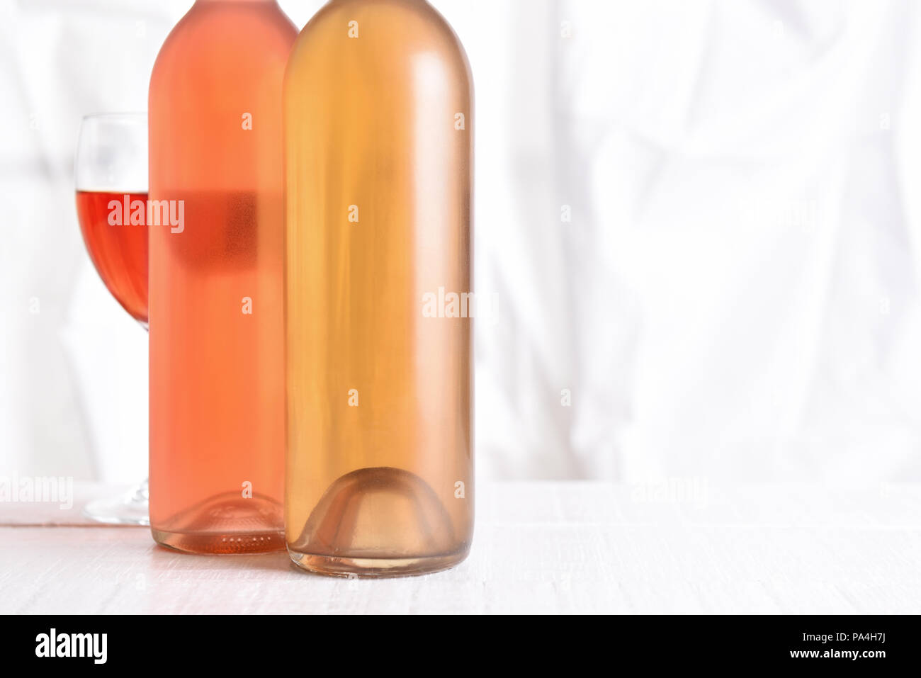 Wine Still Life: High key wine bottles on a white wood table in front of a window. Stock Photo