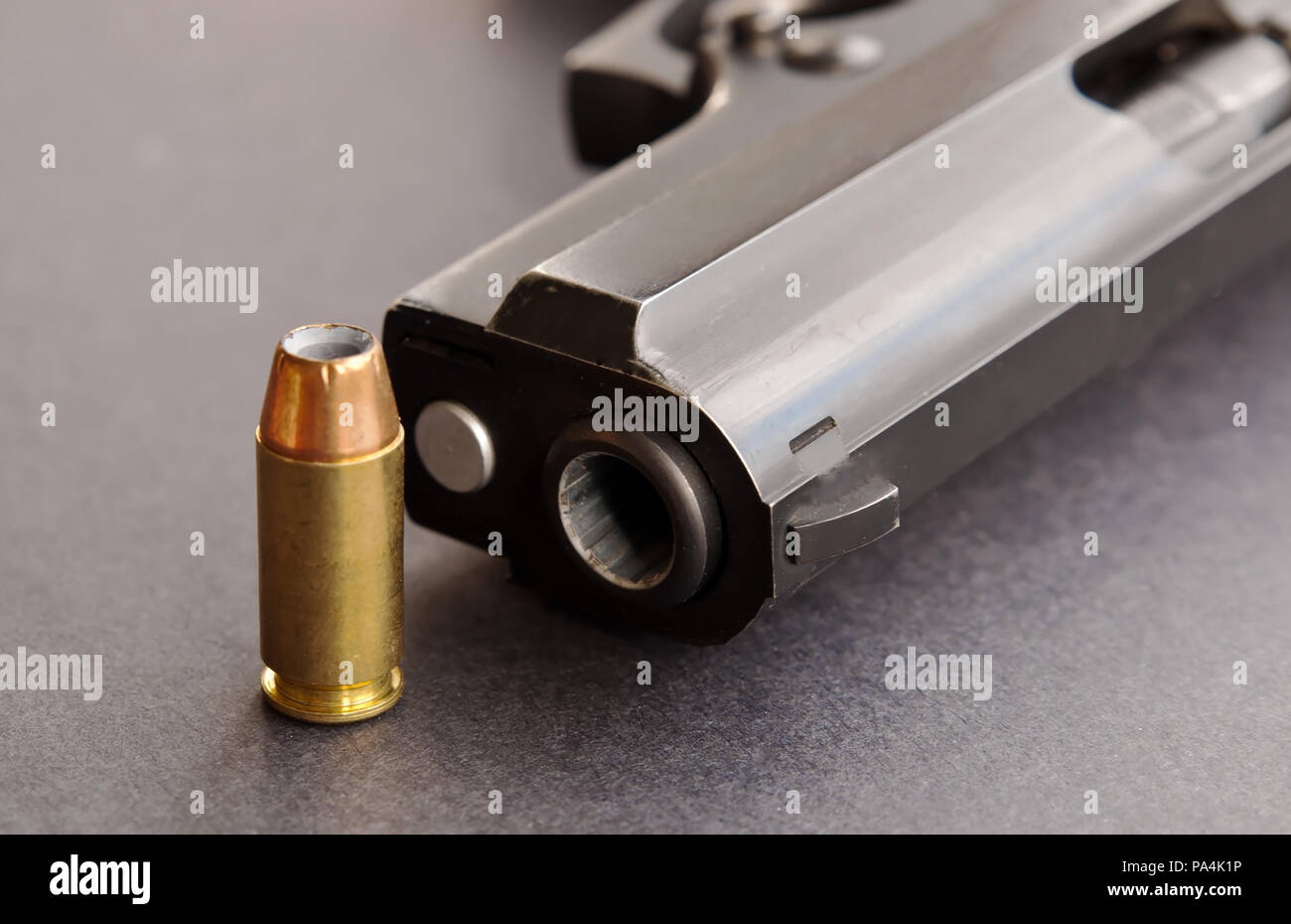 A single 40 caliber hollow point bullet standing next to the muzzle of a black pistol on a black background Stock Photo