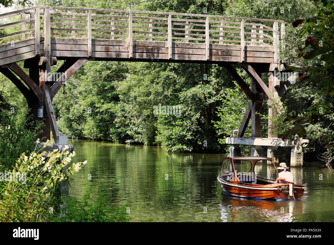 wooden footbridge over the river Thames at Hurley with lady in a motor launch going underneath Stock Photo