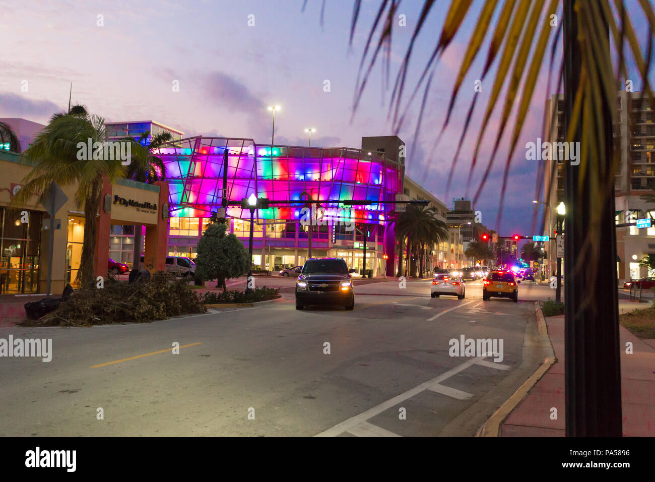TD Bank, lit up at dawn with multicoloured lights, Collins Avenue, Miami Beach, SUV turning a corner with headlights on Stock Photo
