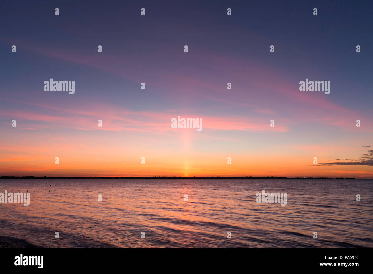 A sun pillar or light pillar at sunset seen from Seasalter, Whitstable, Kent, UK looking across the Swale Estuary towards the Isle of Sheppey. Stock Photo