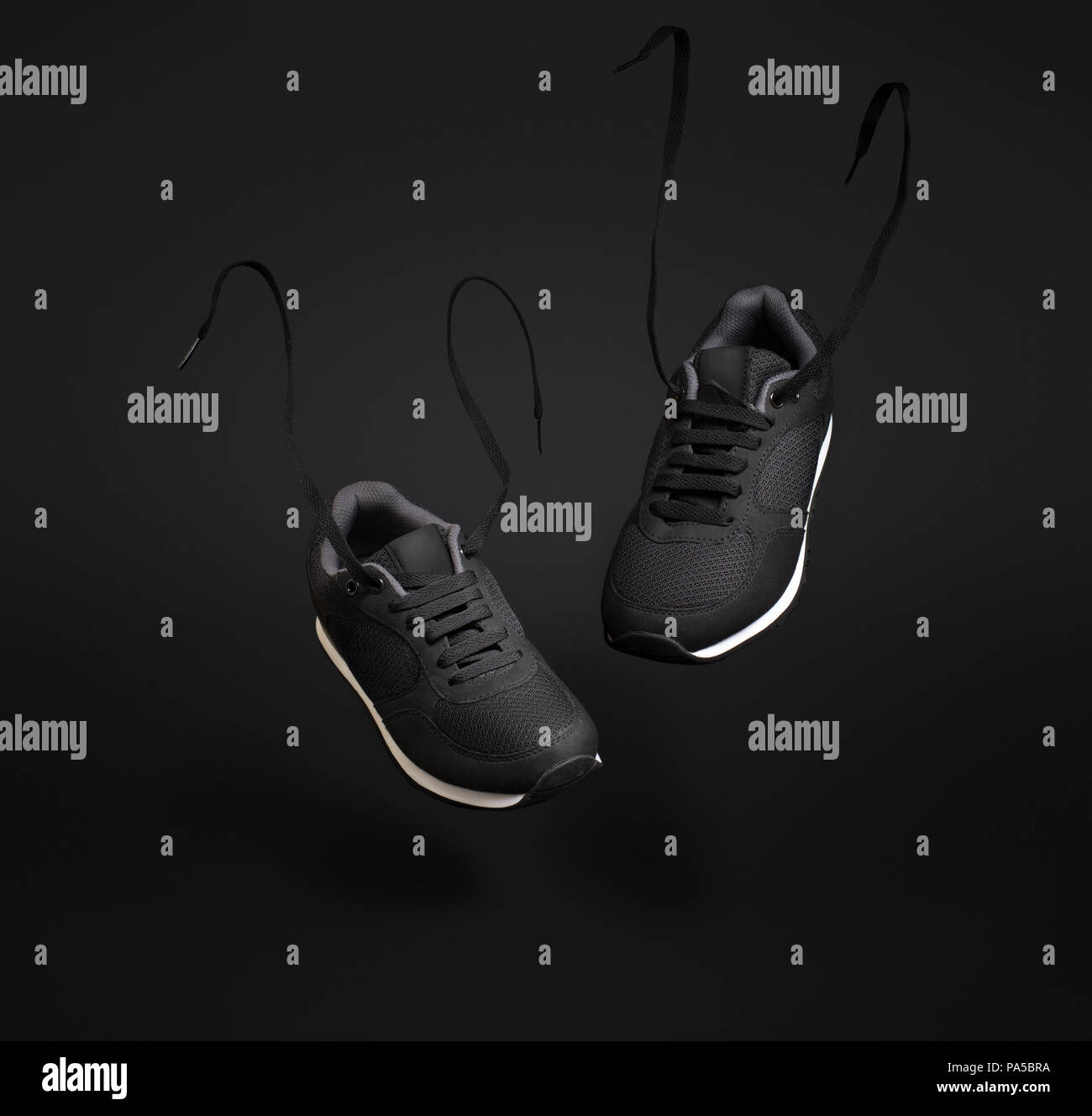 A pair of black unbranded sneakers floating in front of dark background. Stock Photo