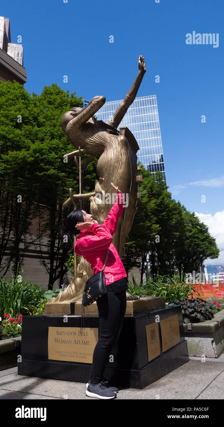 Tourist mimicking bronze street statue by bending back and lifting left hand elegantly just like