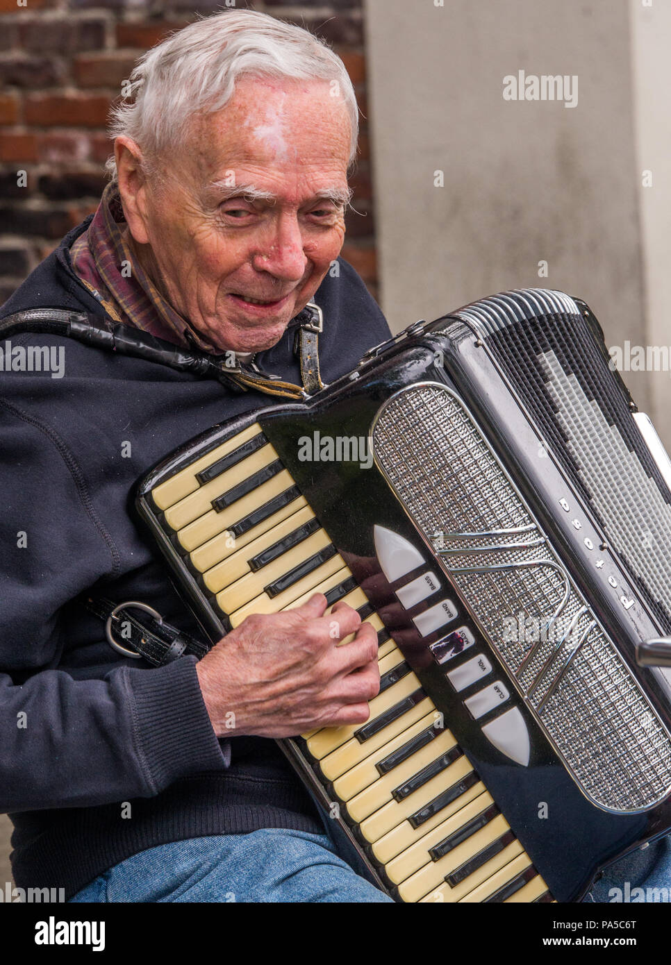 Gray haired jovial old man playing a black, steel and ivory keyed  accordion and singing at farmers market in Seattle Washington. Stock Photo
