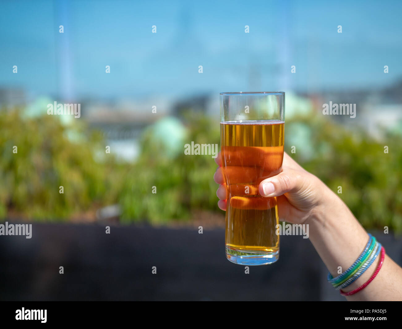 Hand holding glass of beer on a sunny day in festive setting Stock Photo