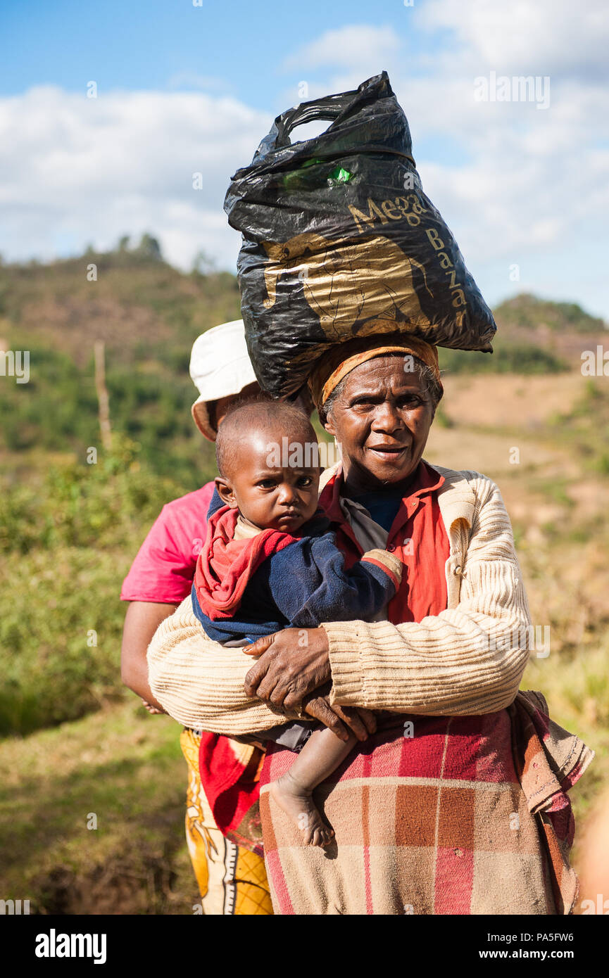 ANTANANARIVO, MADAGASCAR - JUNE 30, 2011: Unidentified Madagascar woman carries her child and some other things the street. People in Madagascar suffe Stock Photo