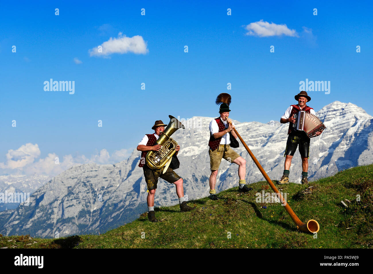 Three folk musicians play in front of mountain panorama, Bergfexn trio in traditional costume on the Eggenalm Stock Photo