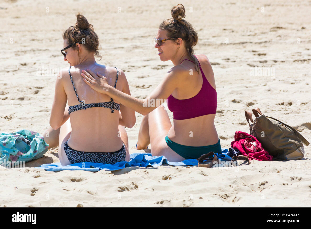 Bournemouth, Dorset, UK. 21st July 2018. UK weather: hot and sunny at Bournemouth beaches, as sunseekers head to the seaside to soak up the sun at the start of the summer holidays. Time to rub more suntan lotion cream in! Two young women sunbathing on the beach. Credit: Carolyn Jenkins/Alamy Live News Stock Photo