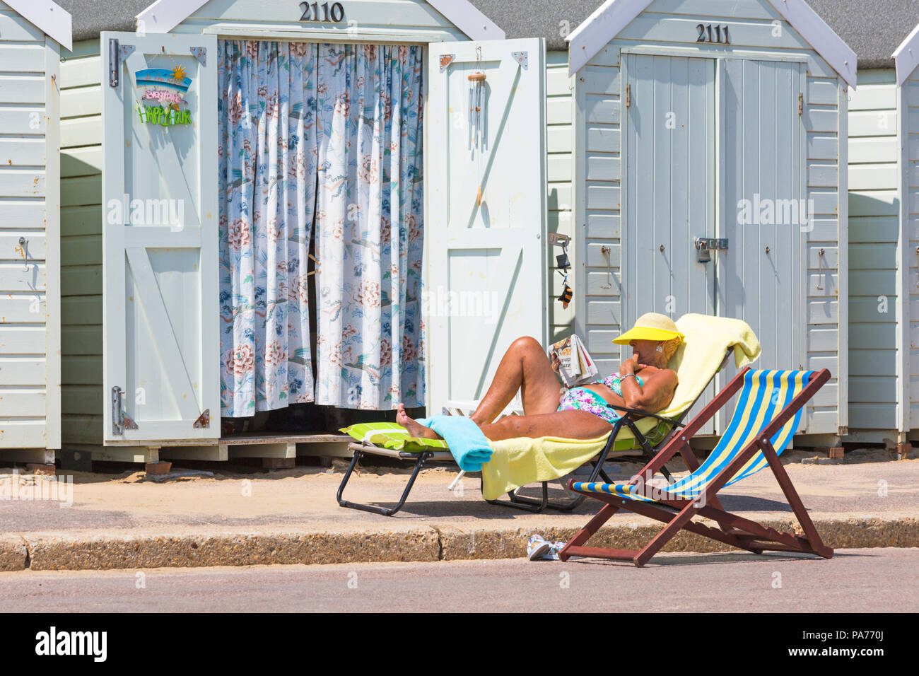 Bournemouth, Dorset, UK. 21st July 2018. UK weather: hot and sunny at Bournemouth beaches, as sunseekers head to the seaside to soak up the sun at the start of the summer holidays. Senior woman sunbathing reading newspaper on sunlounger outside beach huts. Credit: Carolyn Jenkins/Alamy Live News Stock Photo