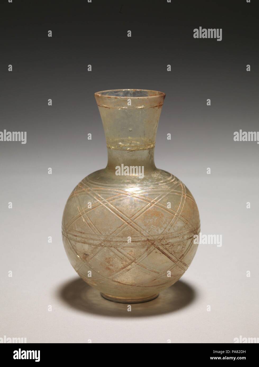Glass flask. Culture: Roman. Dimensions: H.: 5 3/16 in. (13.2 cm). Date: 4th century A.D..  Colorless with pale green tinge.  Plain, vertical rim, ground flat; funnel-shaped neck; globular body; small, flattened bottom.  On neck, two horizontal bands of wheel-cut grooves comprising a single line below rim and a double line two-thirds of way down neck; on body, two concentric grooves around shoulder, a band of three horizontal grooves around body at point of greatest diameter, and two more concentric grooves near base of side; between the uppermost and lowest bands, a further eight bands of dou Stock Photo