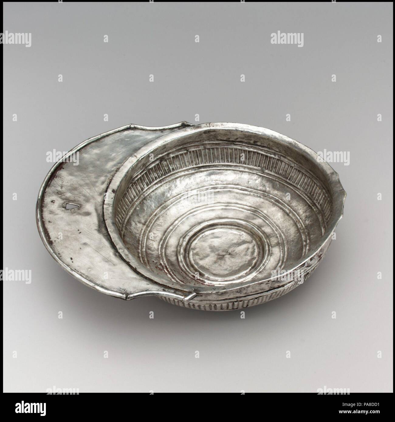 Silver Drinking Bowl with Handle. Culture: Avar. Dimensions: 2 × 9 15/16 × 7 5/16 in., 9.613 Troy Ounces (5.1 × 25.2 × 18.5 cm, 299g)  Other (diameter of cup only): 7 5/16 in. (18.5 cm). Date: 700s.  The Avars  The Avars were a nomadic tribe of mounted warriors from the Eurasian steppe. The Byzantine emperor Justinian negotiated with them in the sixth century to protect the Empire's northern border along the Black Sea. Emboldened by their subjugation of numerous tribes, they unsuccessfully attempted to seize the Empire's capital, Constantinople. They remained a scourge of both Byzantium and th Stock Photo