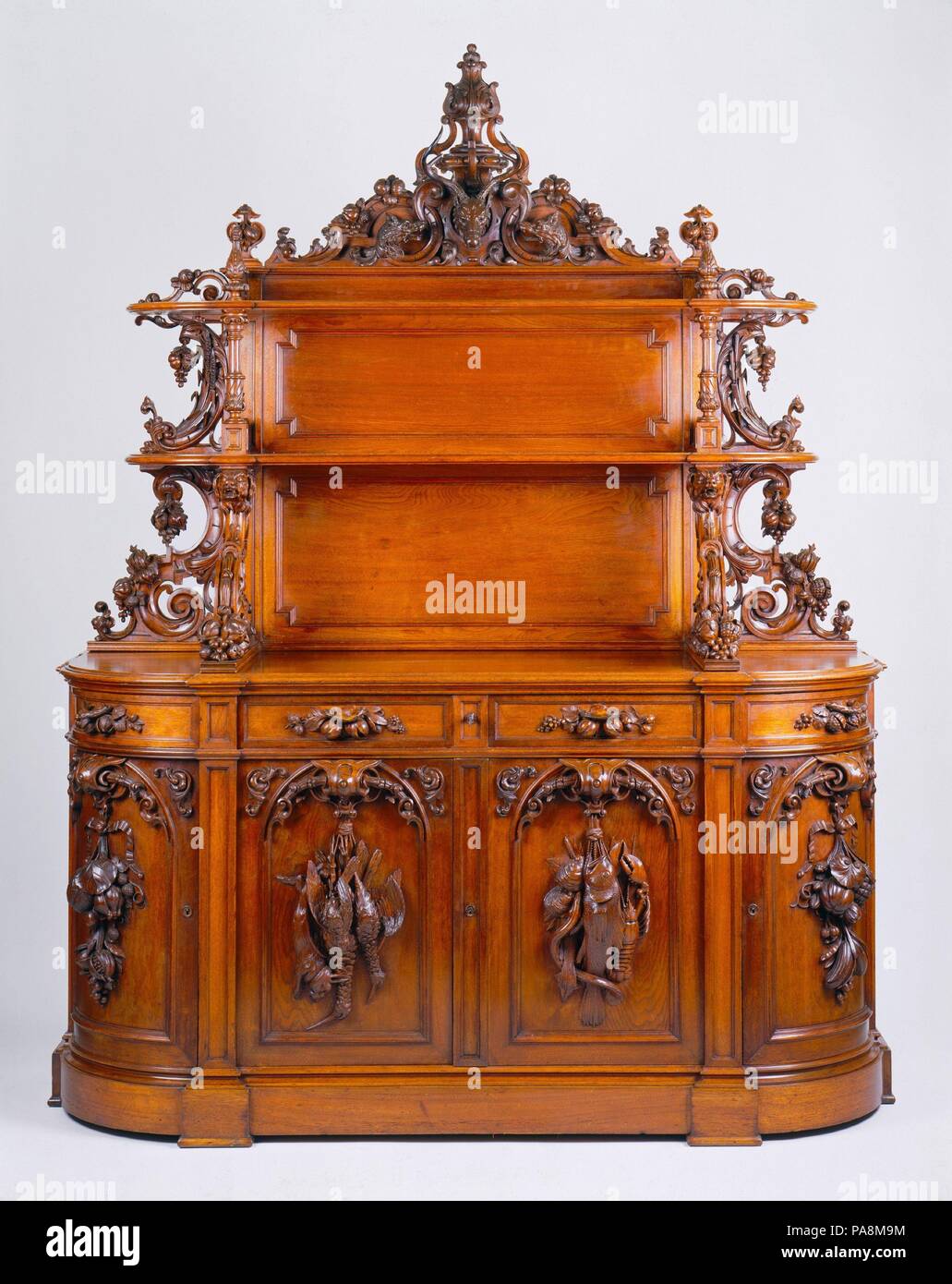 Sideboard. Culture: American. Dimensions: 92 3/4 x 71 3/4 x 25 5/8 in. (235.6 x 182.2 x 65.1 cm). Maker: Alexander Roux (1813-1886). Date: ca. 1853. This sideboard by Aleander Roux is an "etagere" type, with an upper structure of shelves meant for the display of dining ware. Sometimes dubbed "the altar of gastronomy," the form became popular in America and Eurpoe about 1850 and remained a prominent feature of dining rooms for the next quarter century. Hunt and harvest themes prevailed. Roux displayed the prototype for this piece at the 1853 Crystal Palace Exhibition in New York. Afterward, he Stock Photo