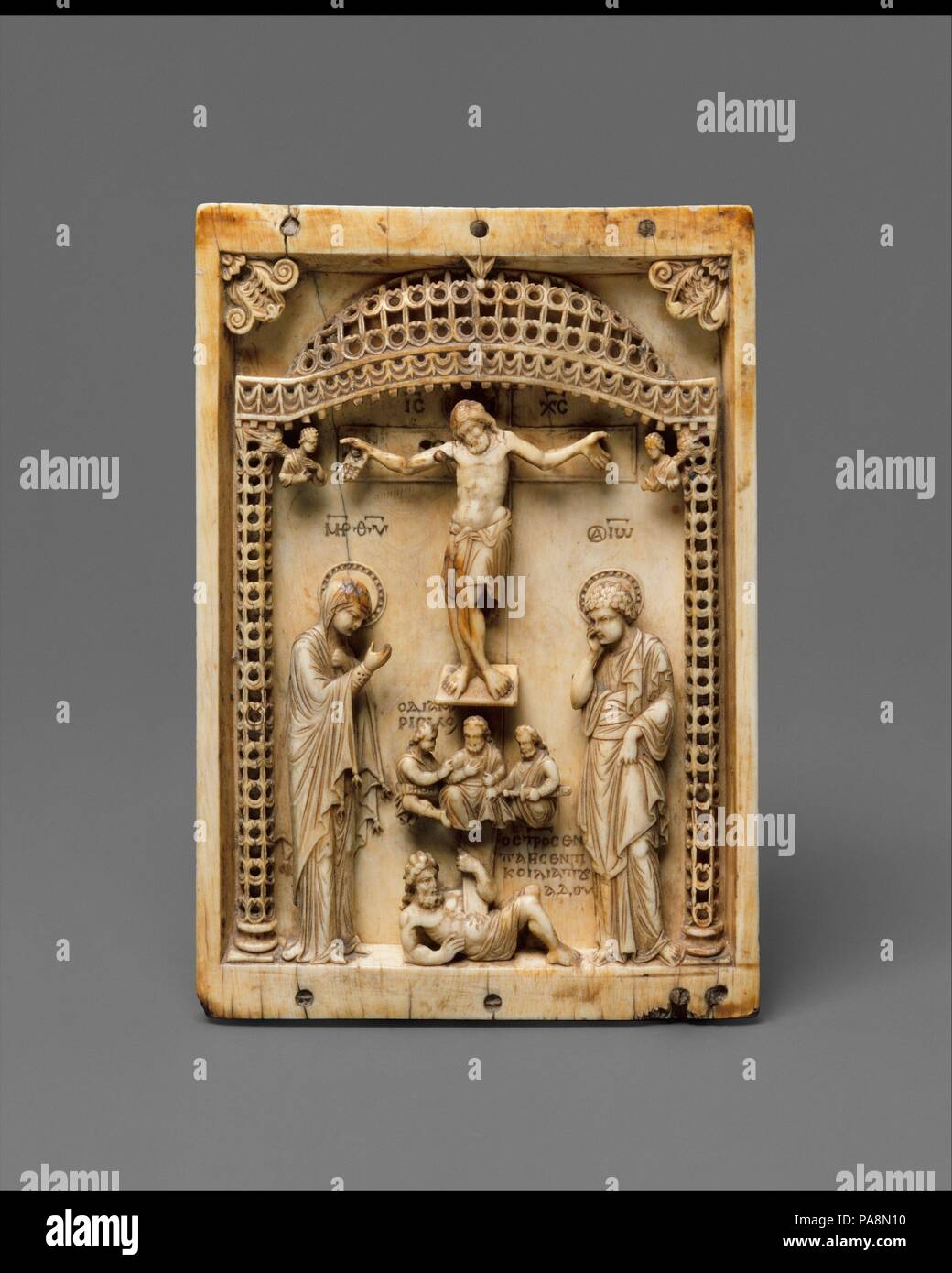 Icon with the Crucifixion. Culture: Byzantine. Dimensions: 5 15/16 × 3 1/2 × 5/16 in. (15.1 × 8.9 × 0.8 cm). Date: mid-10th century.  This Byzantine depiction of the Crucifixion emphasizes Christ's victory over death.  Christ's body is shown limply attached to the cross, his arms bent at the elbows and his legs turned, pushing his hip slightly outward.  His head falls forward against his left shoulder.  The Virgin and Saint John the Baptist mourn his passing, and underneath the foot support, the three soldiers divide Christ's seamless garment.  These figures are frequently portrayed as witness Stock Photo